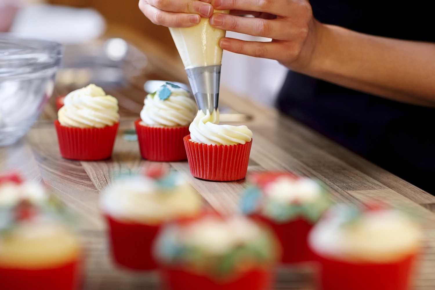 Hands piping icing onto cupcakes in a kitchen